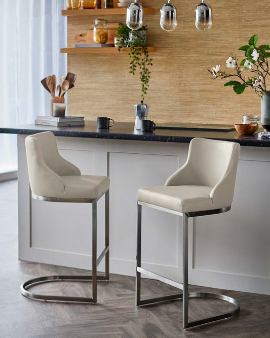 Two modern bar stools with curved backs and cream upholstery, featuring sleek metal frames, displayed at a stylish kitchen counter.