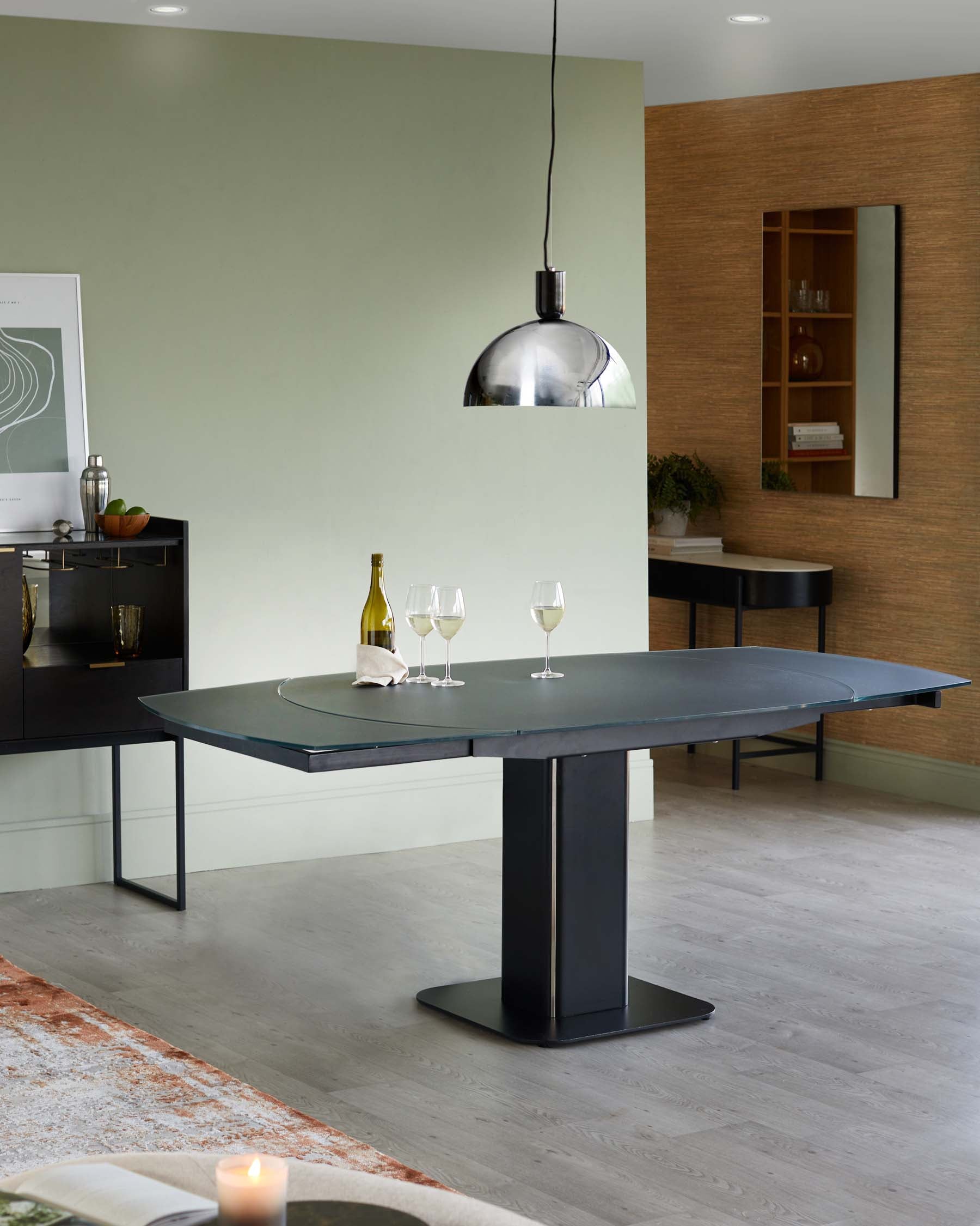 A modern black dining table with a unique pedestal base, paired with elegant glassware and a stylish pendant light above.