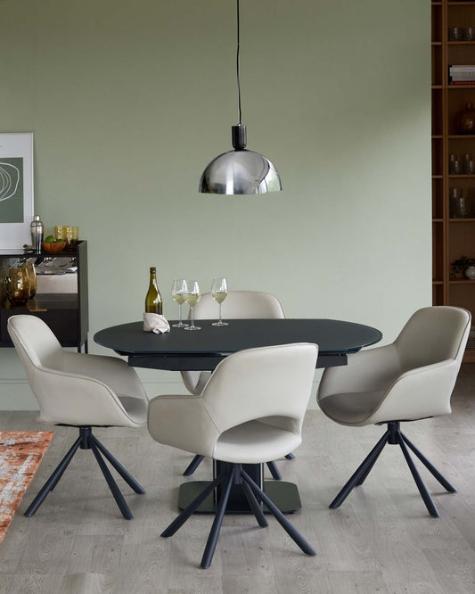 Round black dining table with four light grey upholstered swivel chairs, complemented by a sleek metallic pendant light above.