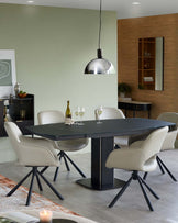 A modern dining table with a black top and pedestal base, surrounded by stylish light beige swivel chairs and a sleek pendant light.