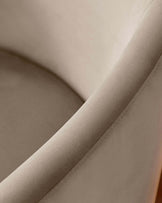 A close-up of a smooth, curved chair in soft beige fabric, highlighting its elegant design and seamless stitching.