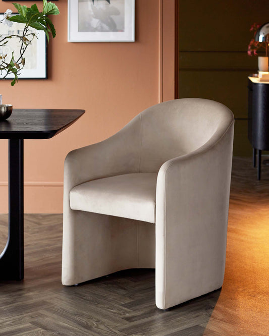 A sleek, curved beige chair next to a black table, complemented by a warm-toned background and decorative art.