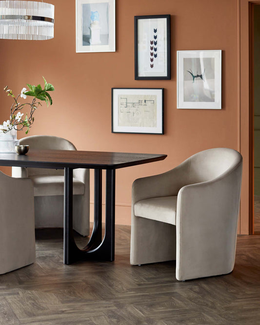 A stylish dining table with a sleek black base, paired with modern beige upholstered chairs, set against a warm, earthy wall.