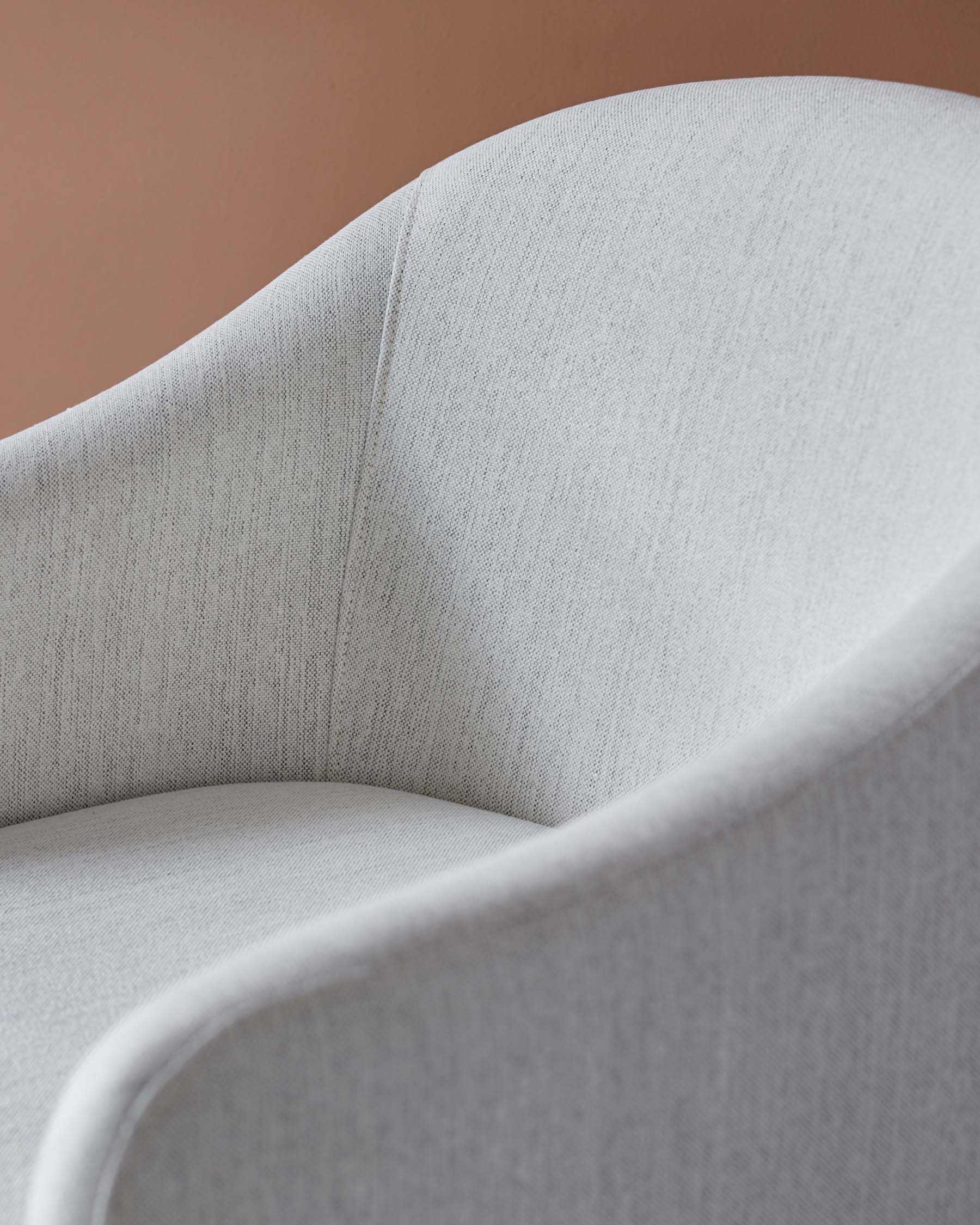 Curved, softly upholstered armchair in light gray fabric, featuring smooth lines and a minimalist design.