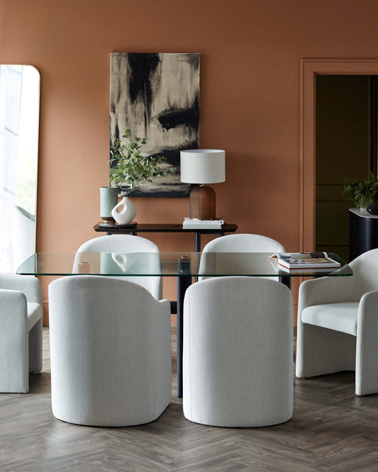 Modern dining set featuring a glass table and four plush, rounded armchairs in light fabric against a warm, earthy backdrop.