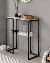 Modern console table with a marble top, glass shelf, black metal frame, and decorative items like vases and candles.