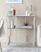 A modern white console table with a glass shelf, accented by vases, books, and decorative items, adding a stylish touch to the decor.