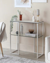 A sleek white console table with glass shelves, decorated with vases, candles, and books, set against a light wall.