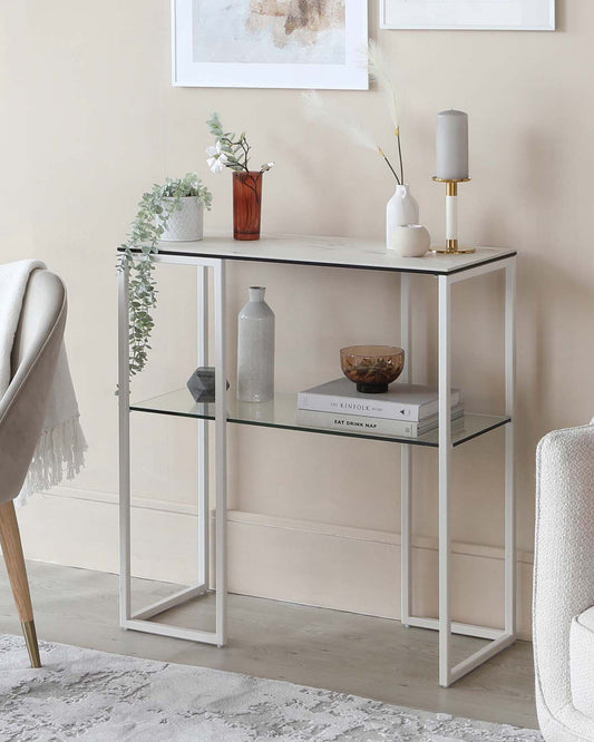 A sleek white console table with glass shelves, decorated with vases, candles, and books, set against a light wall.