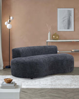 Curvy gray sofa, minimalist side table with decorative items, modern floor lamp, and light rug against a soft pink wall.