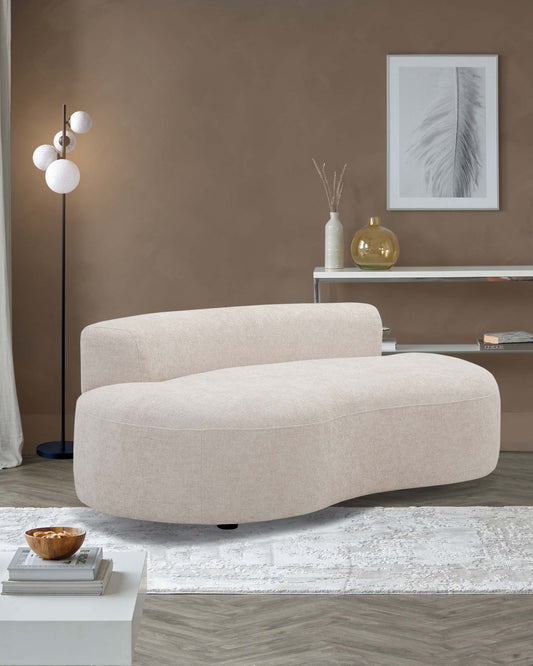 Contemporary beige curved sofa with rounded edges and low-profile black feet, set in a modern living room alongside a sleek white-and-silver console table decorated with vases, a minimalist white coffee table with books and a decorative bowl, atop a textured white area rug, with a backdrop featuring a modern three-sphere floor lamp and a framed feather art piece on a brown wall.