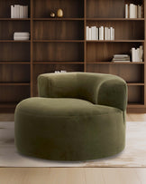 A plush green curved chair with a rounded design, set against a wooden bookshelf and light-colored floor.