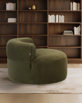 A plush, round green accent chair with a curved back, set against a wooden bookshelf background.