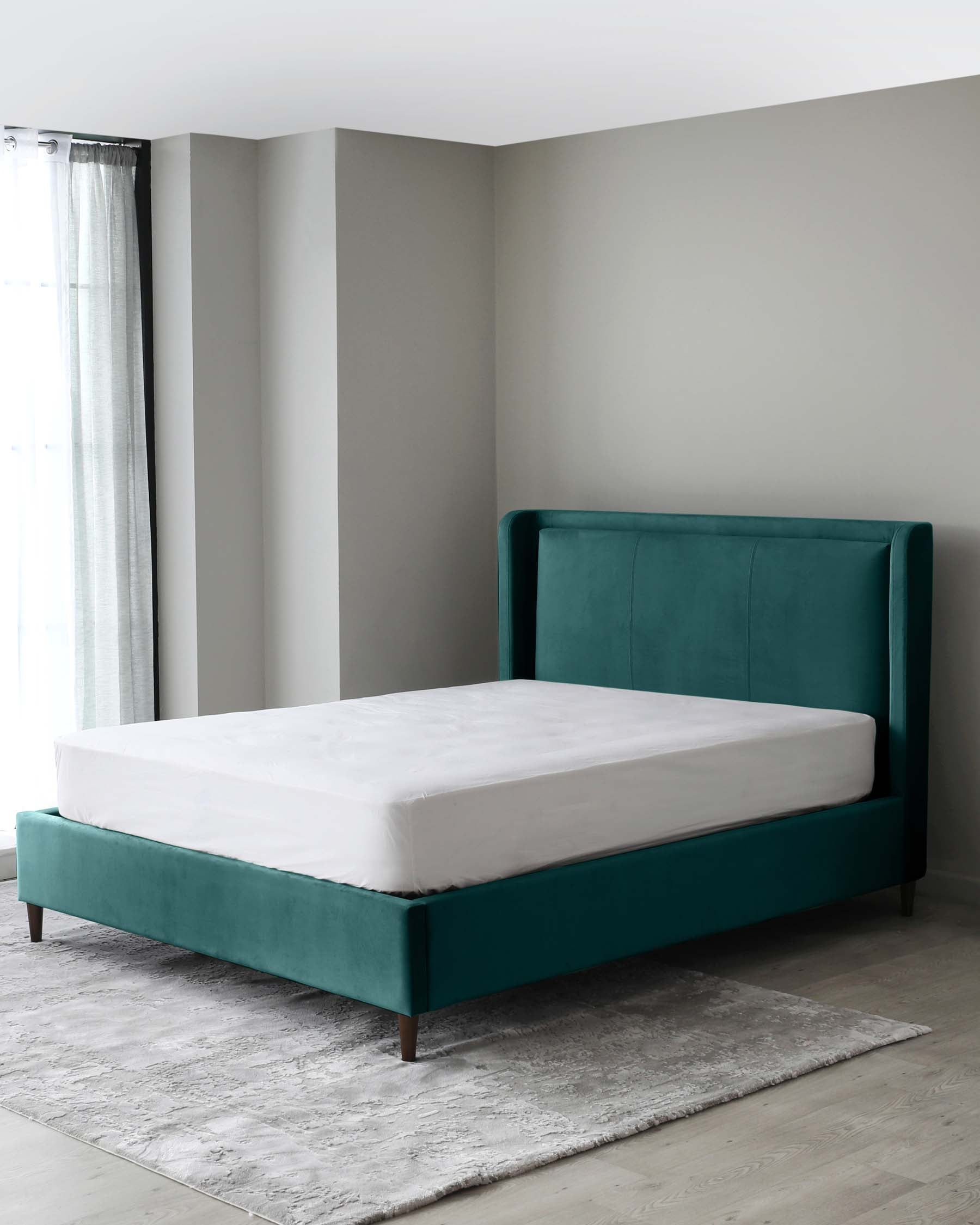 Modern teal upholstered bed frame with a high headboard and wooden legs, accompanied by a white mattress, set on a grey textured area rug over light wooden flooring.