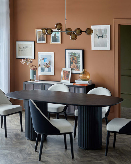 A sleek black oval dining table with a fluted base, complemented by modern chairs featuring a mix of black and light upholstery.