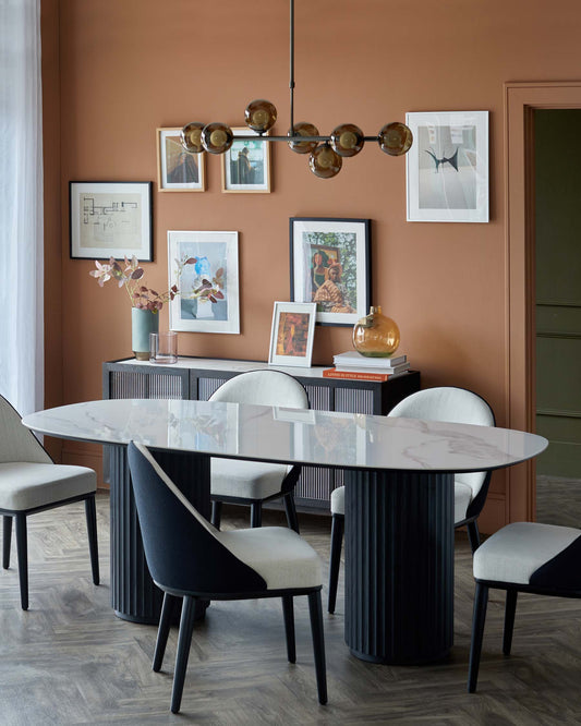 Modern dining set featuring an oval marble table, ribbed black base, and stylish two-tone upholstered chairs under a sleek pendant light.