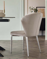 A sleek light beige chair with a curved back and silver legs, paired with a modern black dining table and elegant tableware.