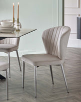 Modern dining chair with a curved back, soft beige upholstery, and sleek metal legs beside a glass table and decorative candles.