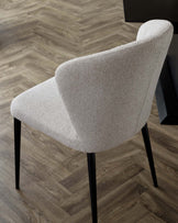 Elegant modern dining chair with a curved backrest, upholstered in textured light beige fabric, complemented by four slender black metal legs.