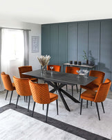 Modern dining set featuring a dark table with a unique base and orange velvet chairs with quilted backs, on a stylish rug.