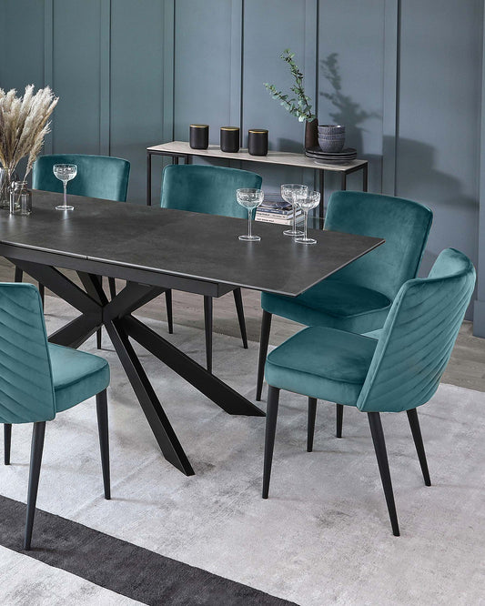 Elegant teal velvet chairs surround a sleek black dining table with an angular base, set on a soft, light-colored rug.