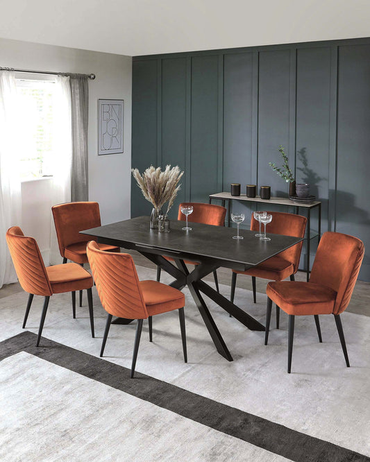 Modern dining set featuring a sleek black table with an angular base and six vibrant orange velvet chairs.