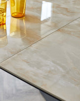 A glossy, light marble dining table featuring warm tones, paired with two transparent yellow drinking glasses.