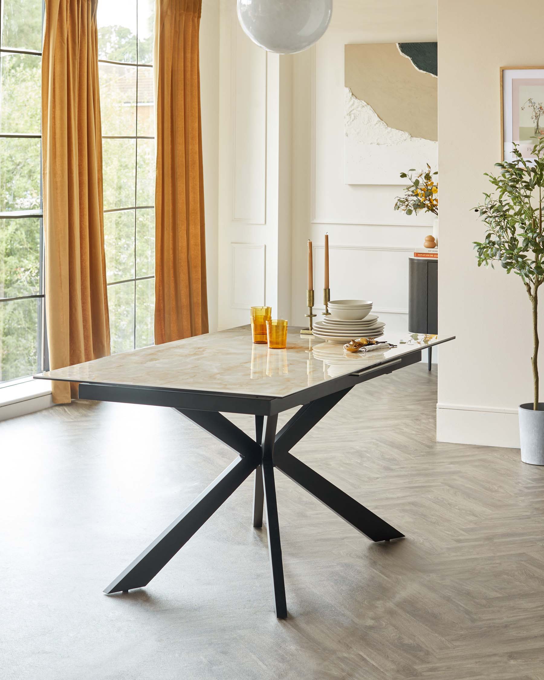 A modern dining table with a marble top and black star-shaped base, accompanied by tableware, candles, and decorative elements.