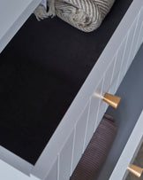 A shallow drawer with a modern design features a gold handle, containing rolled textiles and a textured, neutral-toned throw.