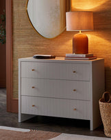 A stylish gray dresser with three textured drawers, paired with a warm lamp and decorative items, set against a textured wall.