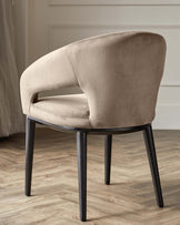 Modern minimalist armchair with soft beige upholstery and black wooden legs on a herringbone-patterned floor.