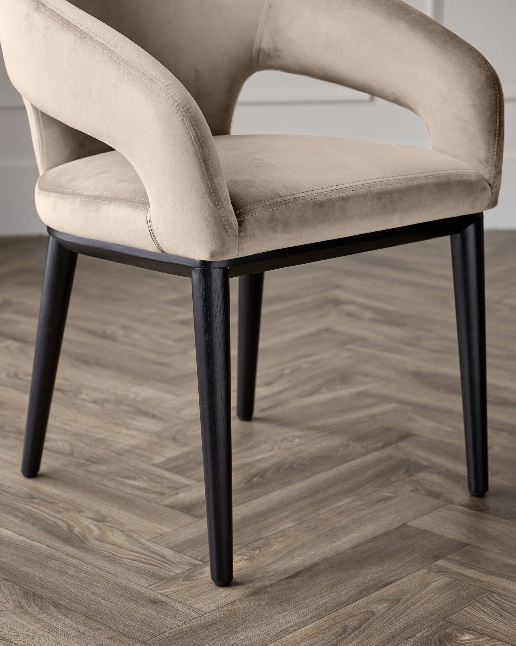 Elegant contemporary dining chair with a curved backrest and plush beige velvet upholstery, featuring slender black wooden legs.