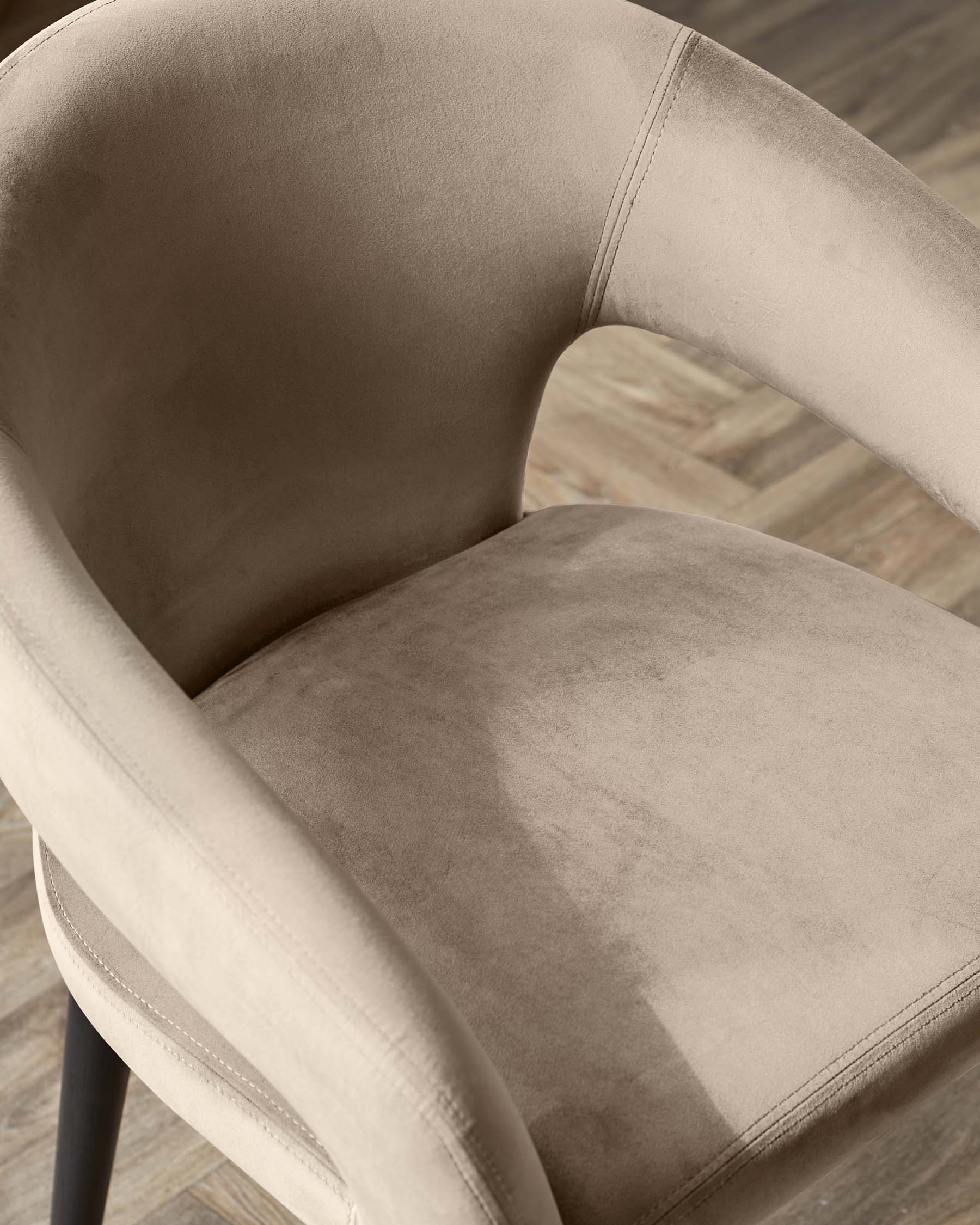 Modern beige upholstered armchair with a curved backrest and seat on a dark wooden base situated on a hardwood floor.