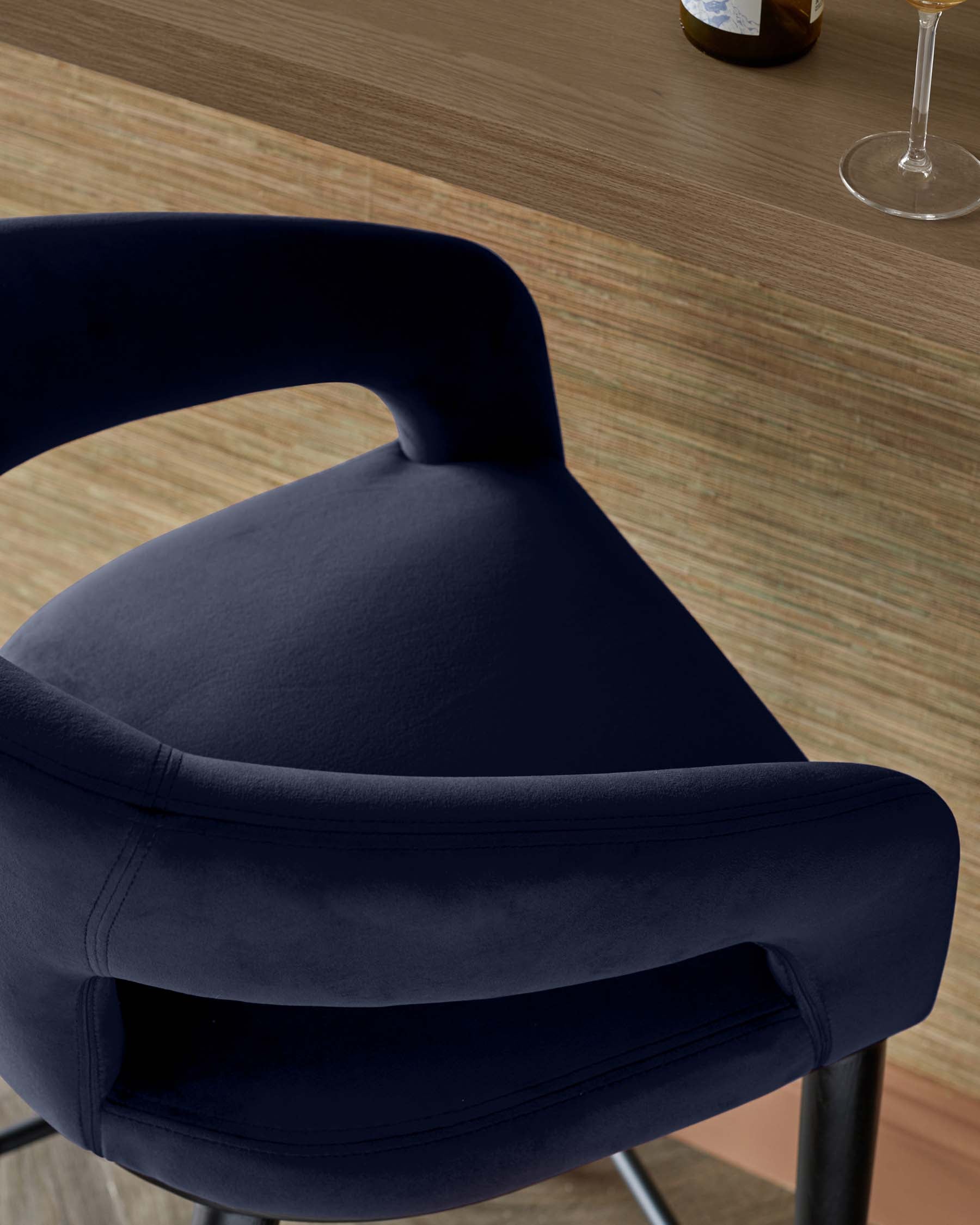 Sleek navy blue upholstered chair with armrests, complemented by a wooden bar top and elegant glassware in the background.