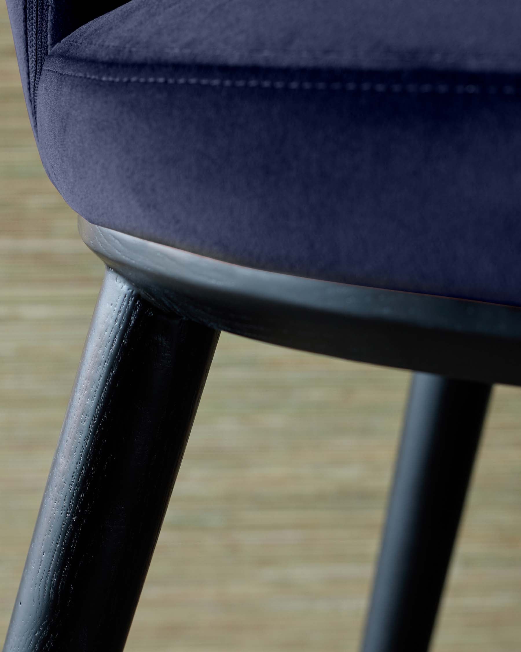 A close-up of a navy velvet chair with sleek black wooden legs, showcasing a modern and elegant design.