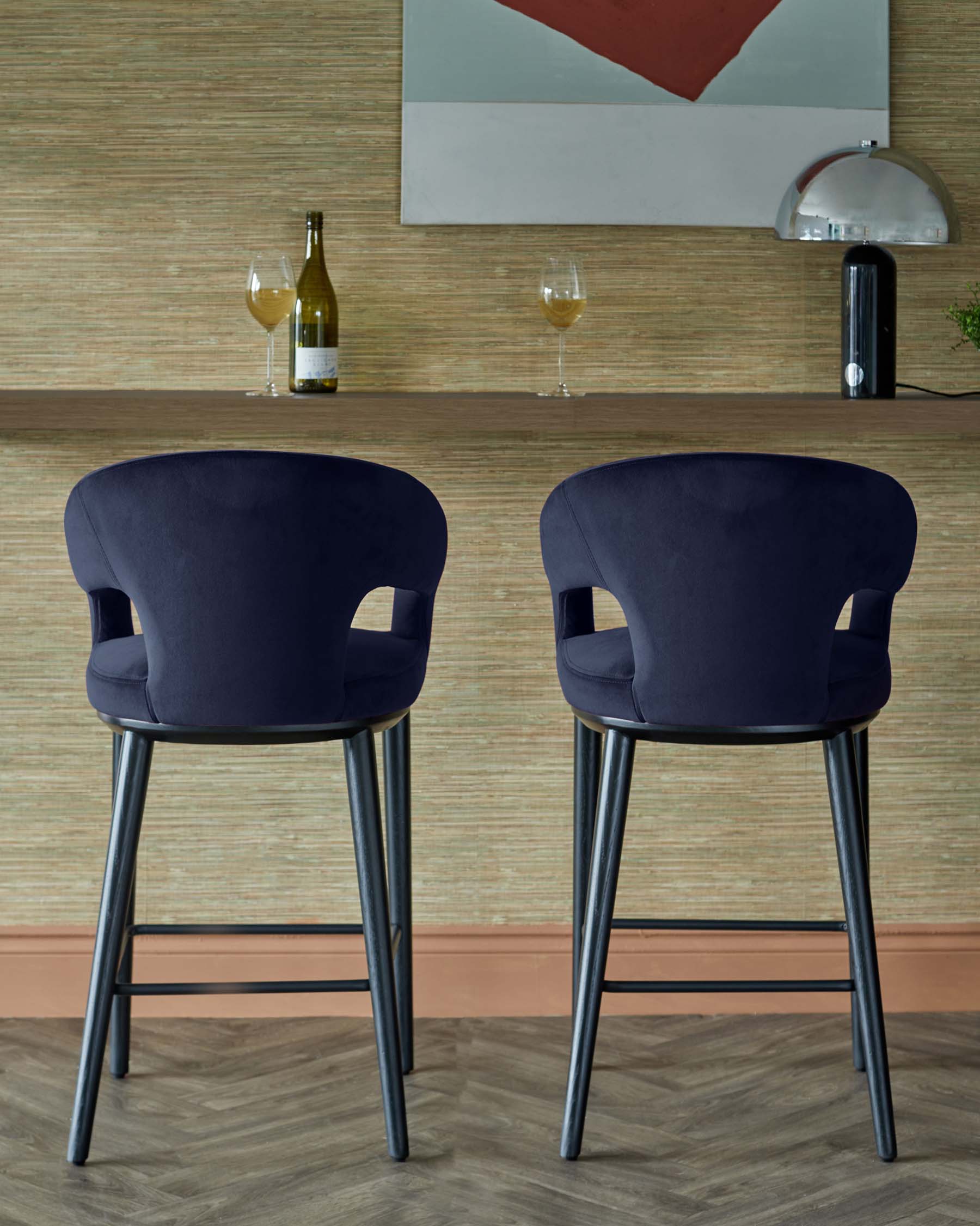 Two elegant navy blue bar stools with rounded backs and black legs, positioned in front of a modern wood shelf with drinks.