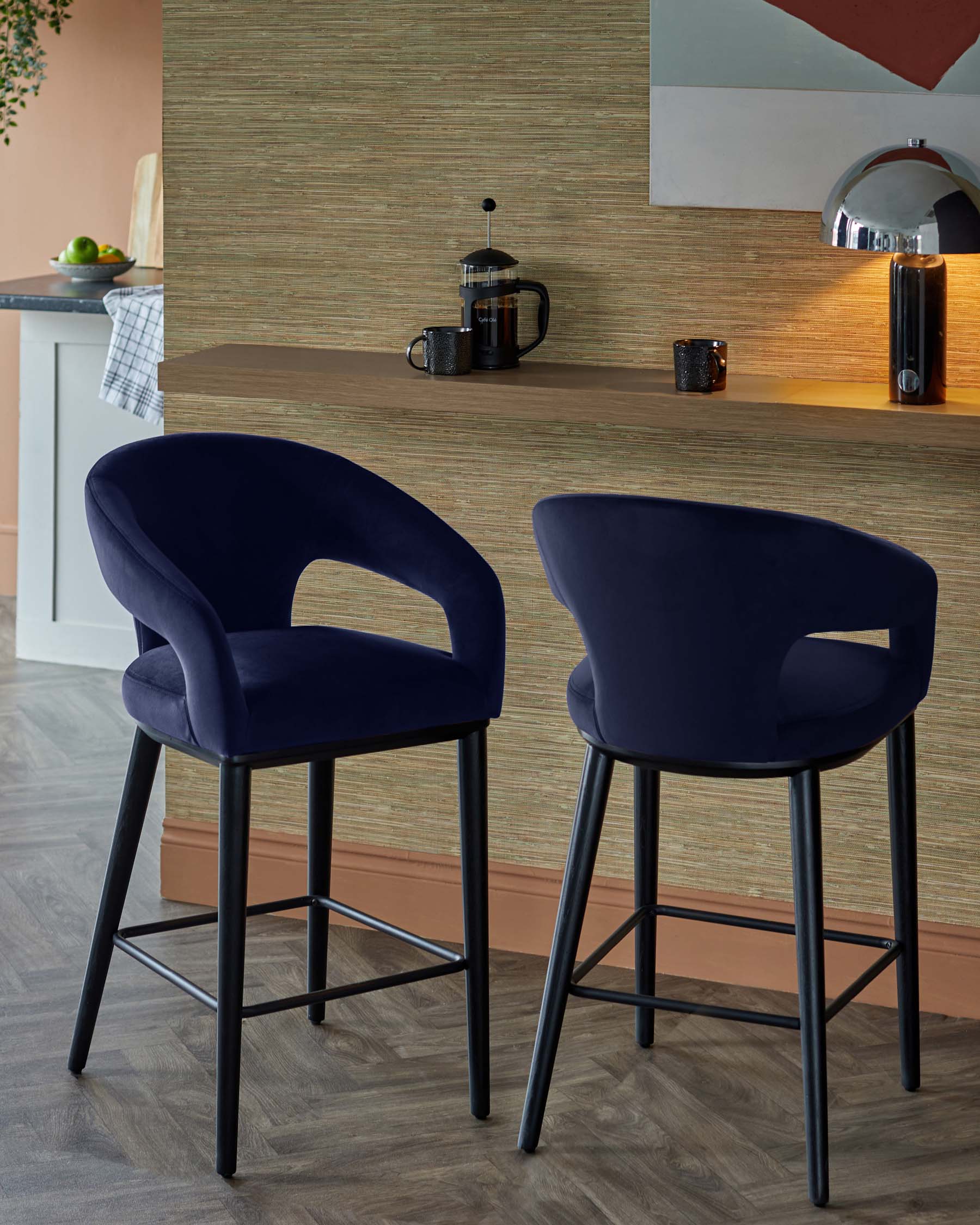 Two stylish navy blue barstools with curved backs and sleek black legs, placed near a modern kitchen bar area.