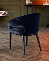 Elegant navy upholstered chair with a curved back and sleek black legs, set against a warm wood floor and contemporary decor.