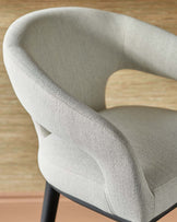 Contemporary curved chair with soft, light gray fabric and sleek black legs, offering a modern and cozy aesthetic.