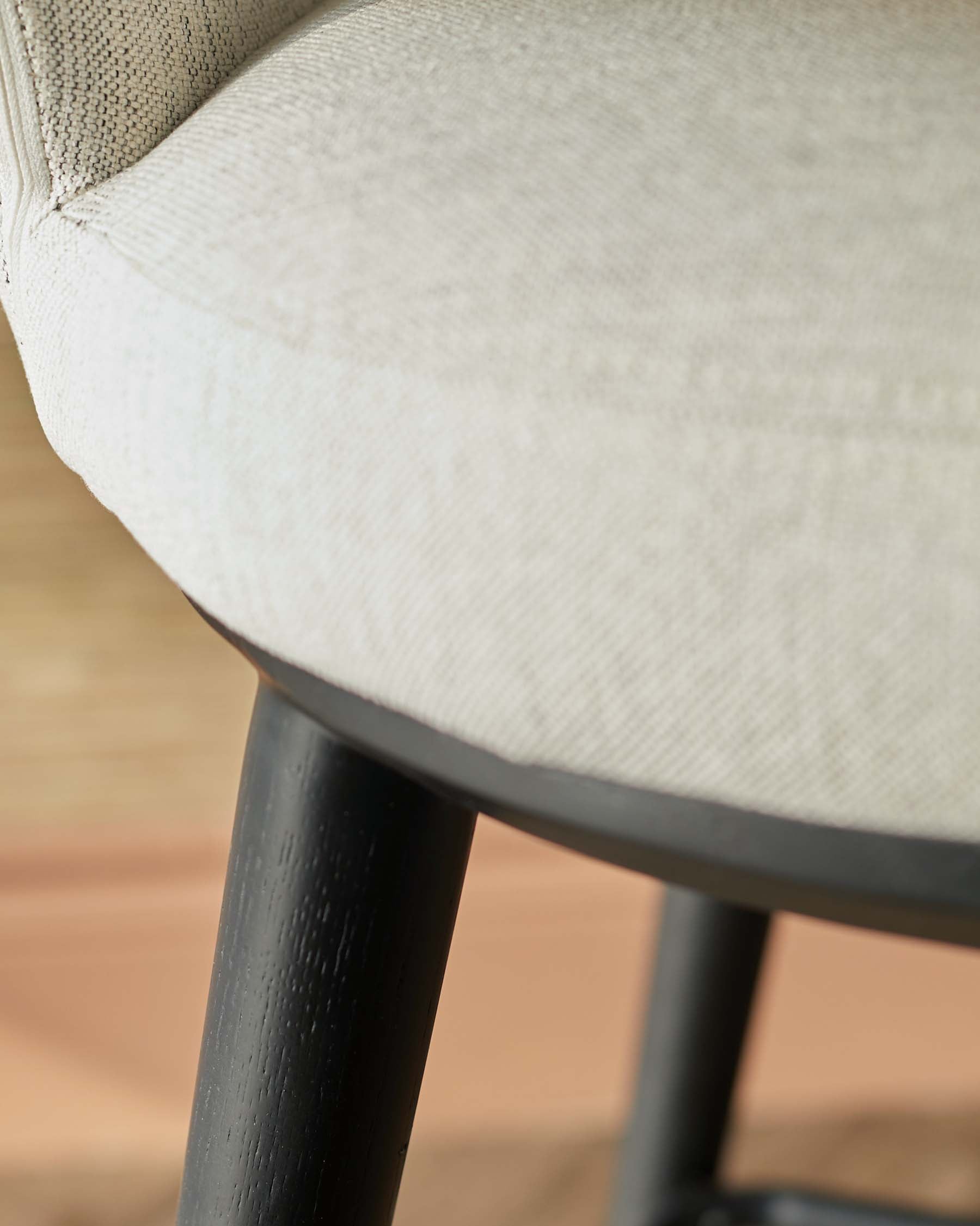 Close-up of a modern chair featuring a soft beige fabric seat and sleek black wooden legs, blending comfort with style.