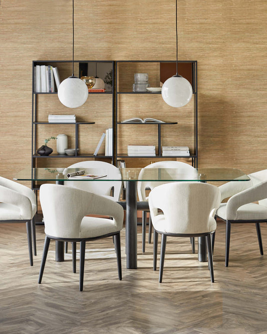 A glass-top dining table with modern, curved cream chairs and a sleek black shelving unit displaying decor and books.