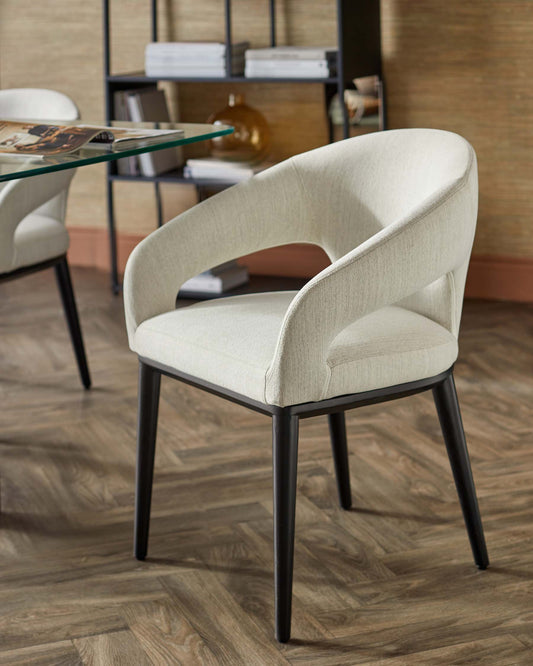 A sleek, modern chair with a curved backrest, upholstered in light fabric, resting on slender black legs.