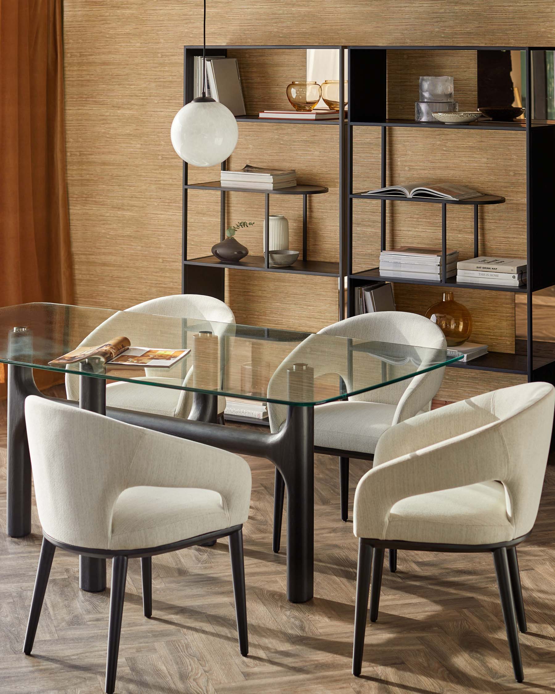 A contemporary glass dining table with elegant, upholstered chairs and a modern shelving unit in a warm-toned interior.