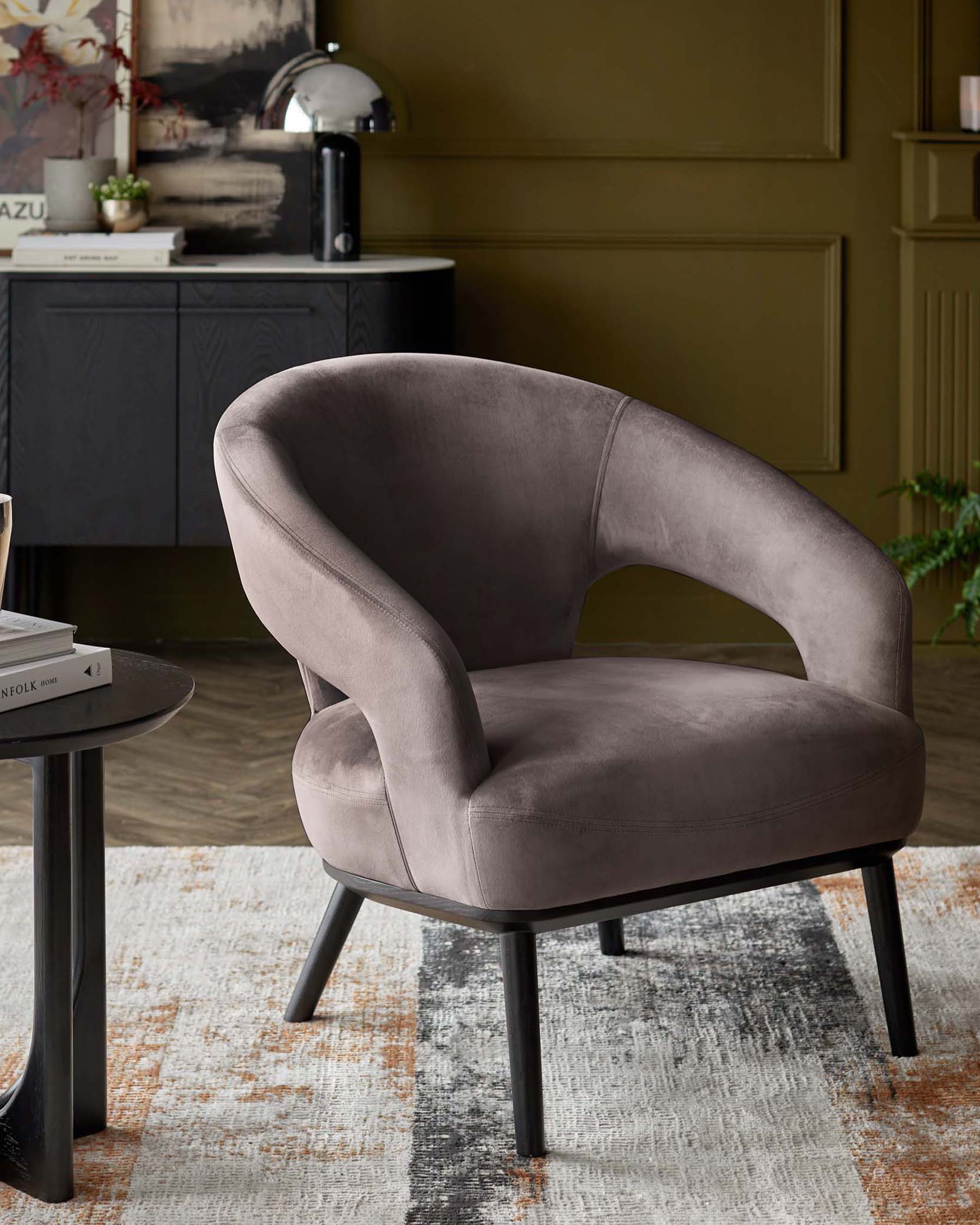 A plush, gray velvet accent chair with a curved back, paired with a sleek black side table and a modern lamp in a stylish setting.