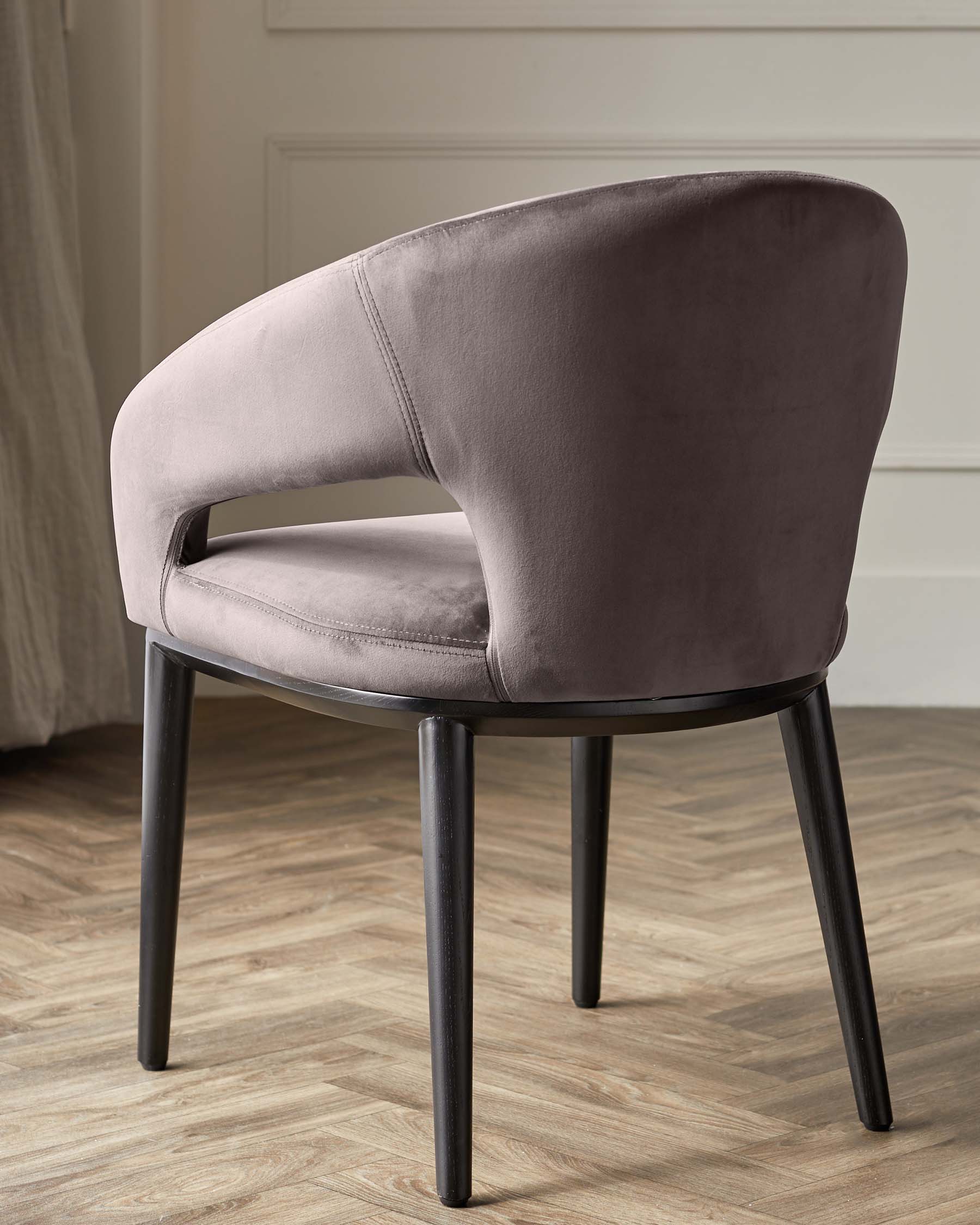 Elegant modern velvet accent chair with a curved backrest and four sleek black angular legs, positioned on a hardwood floor.