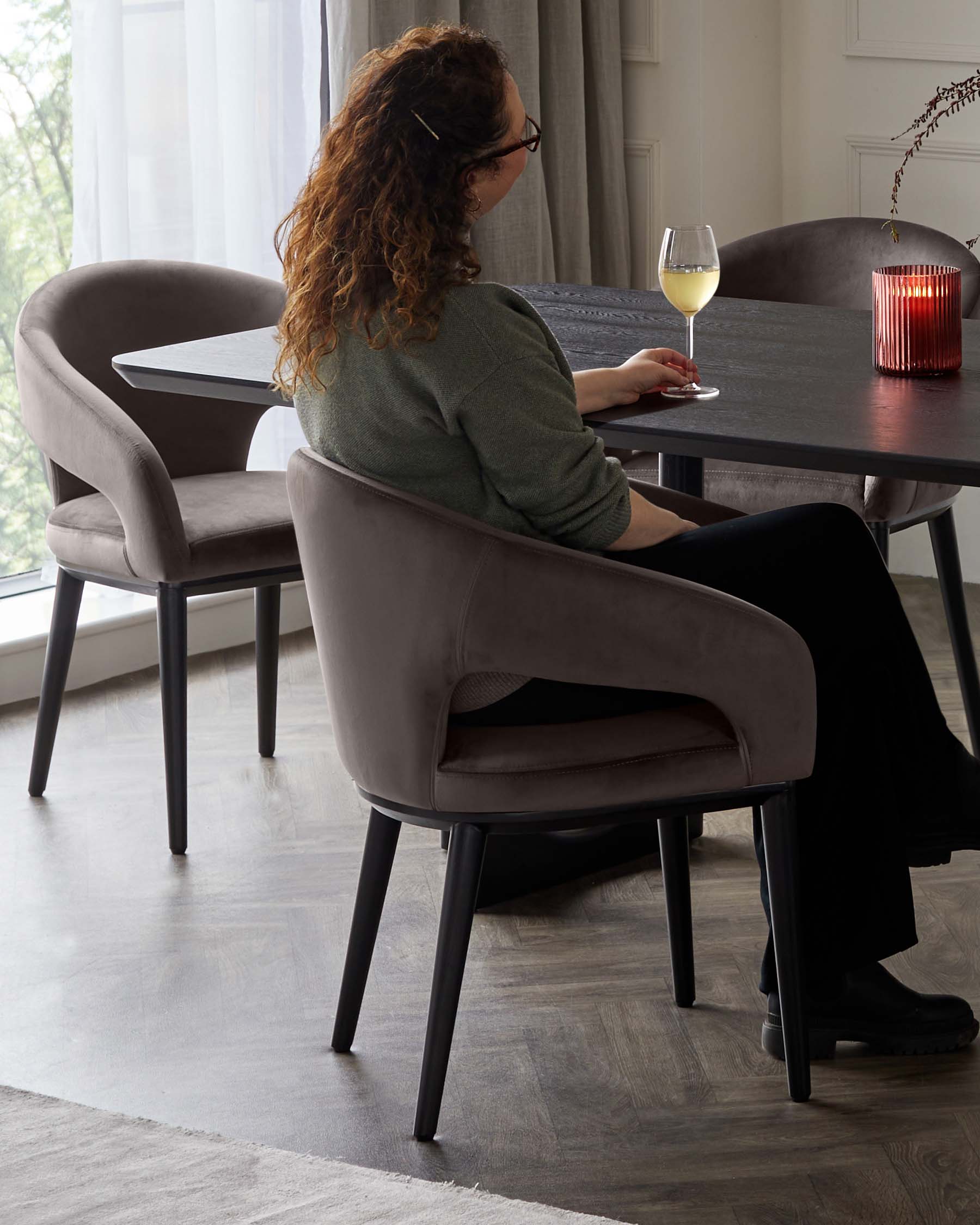 Elegant modern dining set with a textured dark wood round table and plush upholstered dining chairs in a soft grey fabric with a smooth curved design and black legs.