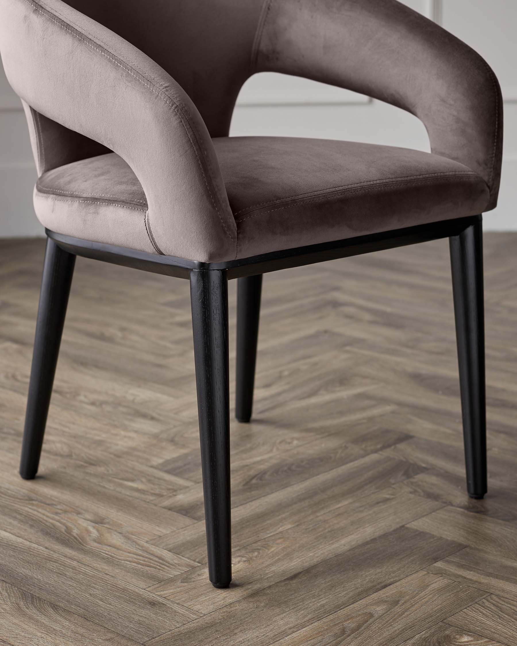 Modern velvet-upholstered dining chair with curved backrest and sleek black wooden legs, set against a herringbone wooden floor.