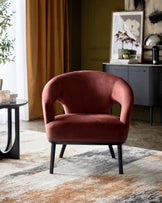 A cozy, deep pink velvet armchair with a curved backrest and slender black legs, positioned on a textured area rug.