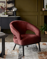 A plush burgundy accent chair with sleek black legs, accompanied by a round side table and a textured rug.