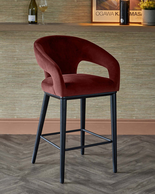 Stylish red velvet bar stool with a curved back and black metal legs, set against a textured wall background.